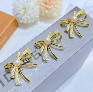 Elegant gold bow brooch set with white crystals and round pearls on a textured background