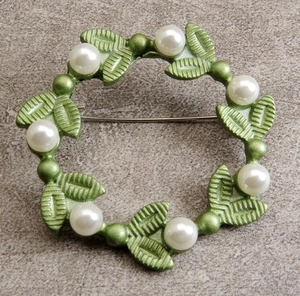 Close-up of circular leaf brooch with white pearls and green textured leaves
