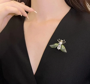 Detail of bee brooch with green wings and crystals worn on black V-neck clothing