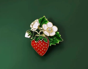 Détail de la broche fraise en émail rouge et petites fleurs blanches sur fond vert foncé