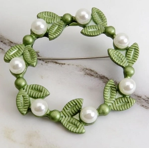 Detailed close-up of a wreath brooch featuring green leaves and white pearls on marble