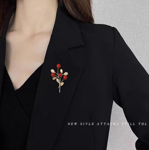 Elegante spilla a foglia dorata con perle rosse e cristalli su un blazer nero