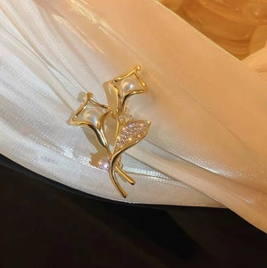 Detailaufnahme einer goldenen Lilienbrosche mit weißen Perlen und Zirkonia-Blättern