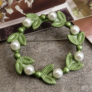 Detail shot of green enamel leaf wreath brooch with white imitation pearls on metal base