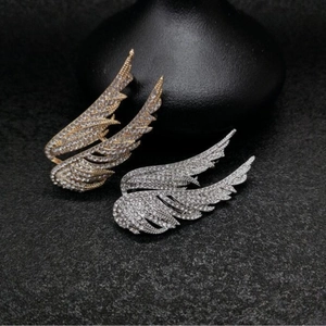 Elegant gold and silver angel wing brooches with sparkling crystals on dark surface