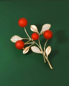 Dettaglio macro di una spilla festiva con bacche rosse, foglie dorate e zirconi