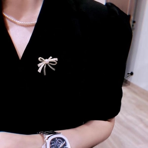Elegant gold bow brooch with pearl and crystals worn on a black dress v-neckline