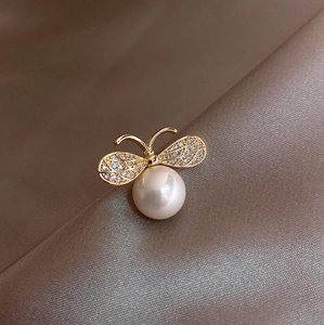 Elegant gold bee brooch with a large white pearl and sparkling crystals on satin background