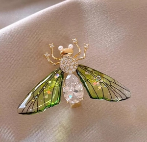 Elegant gold bee brooch with sparkling crystals and translucent green wings on silk
