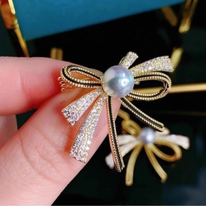 Elegant gold bow brooch with black accents, shimmering crystals and a center pearl