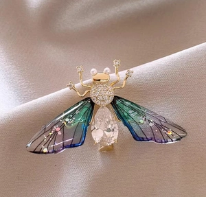Elegant gold cicada brooch with gradient wings and crystals on champagne silk background