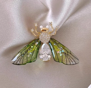 Macro detail of cicada brooch featuring green wings, gold accents and zircon stones