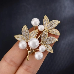 Detailed view of luxury gold leaf brooch with white pearls held in hand for scale