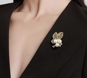 Detail der goldenen Blattbrosche mit weißen Perlen und Kristallen auf schwarzem Blazer