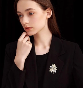 Detailed view of luxury leaf-shaped brooch with white pearls on a black suit jacket