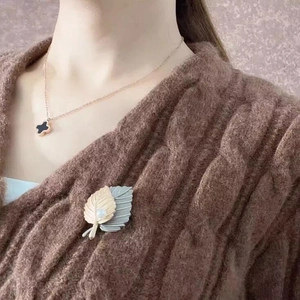Detail shot of vintage leaf brooch with white pearl on brown knitted sweater texture