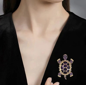 Close-up of a golden turtle brooch with purple rhinestones on a black V-neck dress