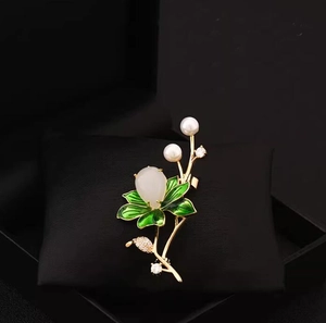 Close-up of elegant lotus brooch with green enamel leaves and white pearls on velvet