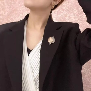 Detail showing a gold maple leaf brooch with white pearl on a black suit jacket