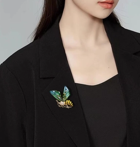 Detail of bee brooch with green enamel wings and zircons on a black blazer lapel