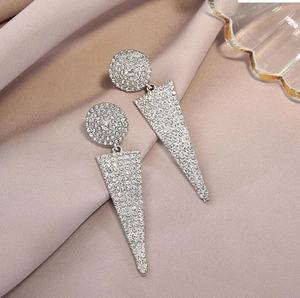 Macro detail of geometric silver earrings with pavé crystals on champagne silk background