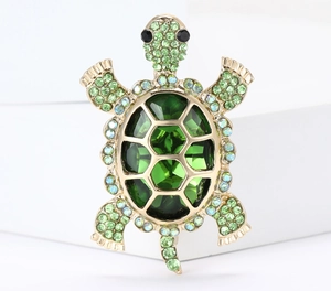 Detailed view of the turtle brooch featuring green crystal shell and gold plating finish
