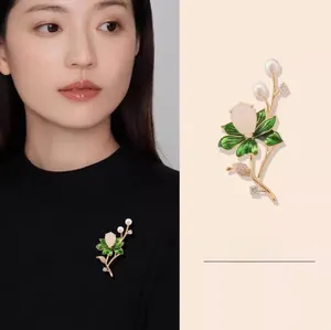 Macro detail of lotus brooch with green enamel, white pearls, and a teardrop gemstone
