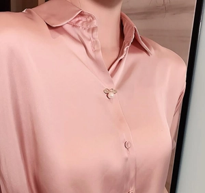 Detail of a pearl bee brooch on a pink satin shirt showing elegant texture and craftsmanship