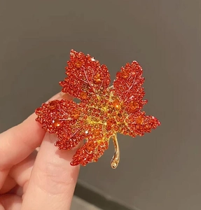 Macro detail of red maple leaf brooch featuring vibrant gradient zircon stones in gold