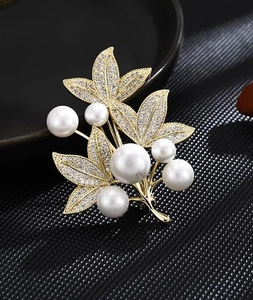 Macro shot of gold leaf brooch with white pearls and sparkling pavé crystal accents