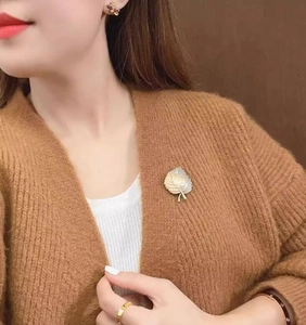 Detail view of retro maple leaf brooch with white pearl on a brown knitted cardigan