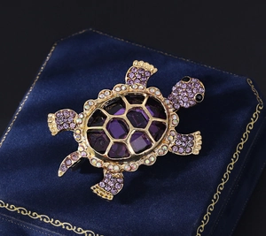 Macro view of gold tortoise brooch with purple crystals on a blue velvet jewelry box