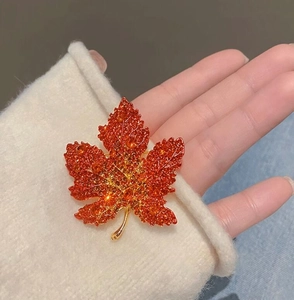 Close-up of red maple leaf brooch with crystal rhinestones on white sweater