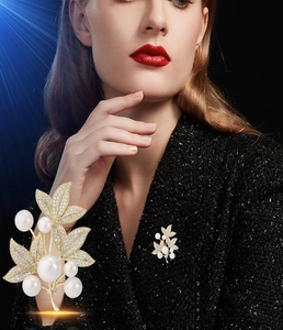 Macro detail of luxury gold leaf brooch with white pearls and crystals on dark coat