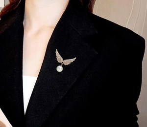 Détail de la broche aile d'ange avec cristaux blancs et perle sur un blazer noir