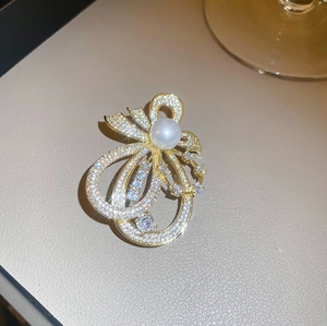 Eleganter goldener Schleifen-Brosche mit Kristallen und weißer Perle auf beigem Grund