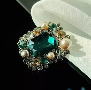 Vintage emerald-cut stone brooch with multi-colored pearls and gems on silk background