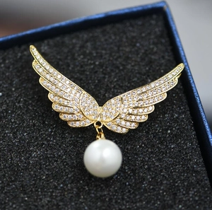 Détail macro de la broche ailes d'ange dorées avec zircons sertis et perle blanche ronde