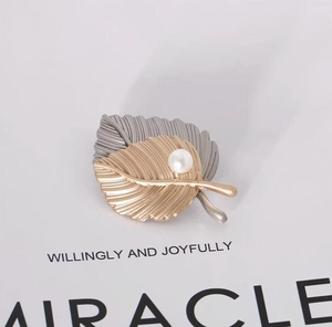 Detail of dual-tone maple leaf brooch with brushed texture and a central white pearl