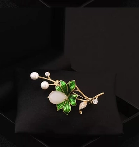 Detailed view of a gold lotus brooch with green enamel leaves and white pearls