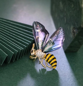Detailed macro view of bee brooch with purple wings and white crystal paving on gold metal