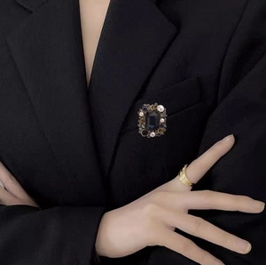 Vintage sapphire square brooch and layered gold ring with pearls on a black suit blazer