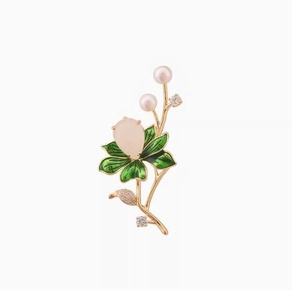Close-up of golden lotus brooch with green enamel leaves and pink gemstone