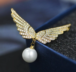 Détail macro d'une broche ailes d'ange avec cristaux brillants et perle ronde
