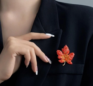 Detailed close-up of a luxury red maple leaf brooch with crystals on a black suit jacket