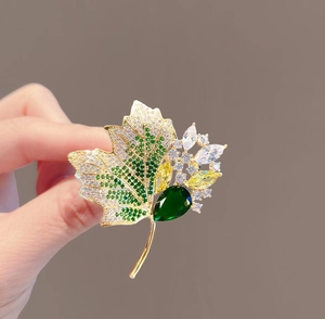 Detailed close-up of a luxury maple leaf brooch with green gemstone and multicolored zircons