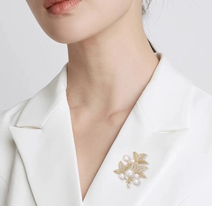 Close-up of golden leaf brooch with white pearls and diamonds on white suit lapel