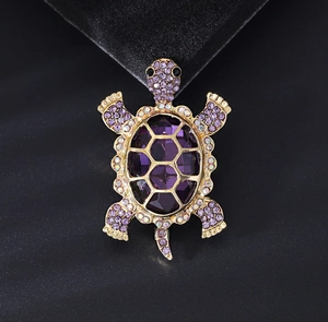 Macro shot of purple gemstone turtle brooch with sparkling gold crystal details