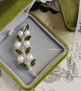 Vue macro d'une broche feuille en émail vert avec perles blanches dans un écrin de velours