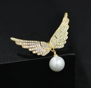 Détail d'une broche ailes d'ange dorées avec zircons étincelants et perle blanche